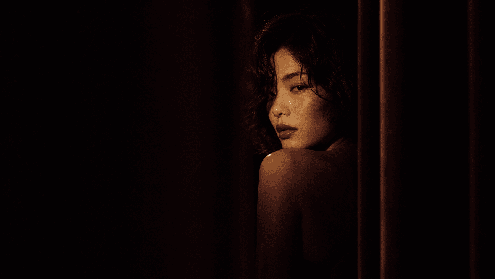 The woman looking back over her shoulder by a dark red curtain