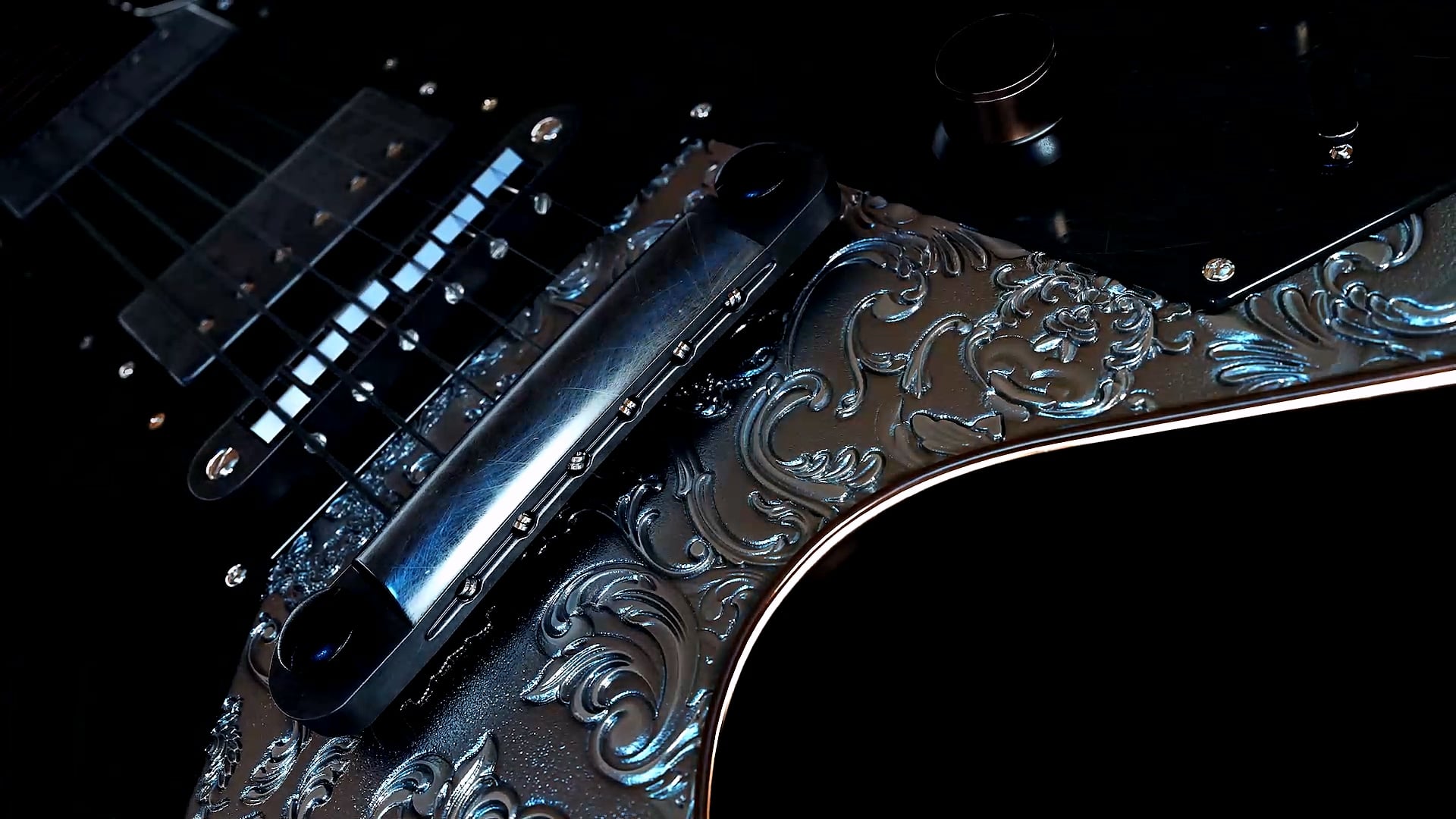 Close-up of an electric guitar with an engraved metal body and chrome pickups.